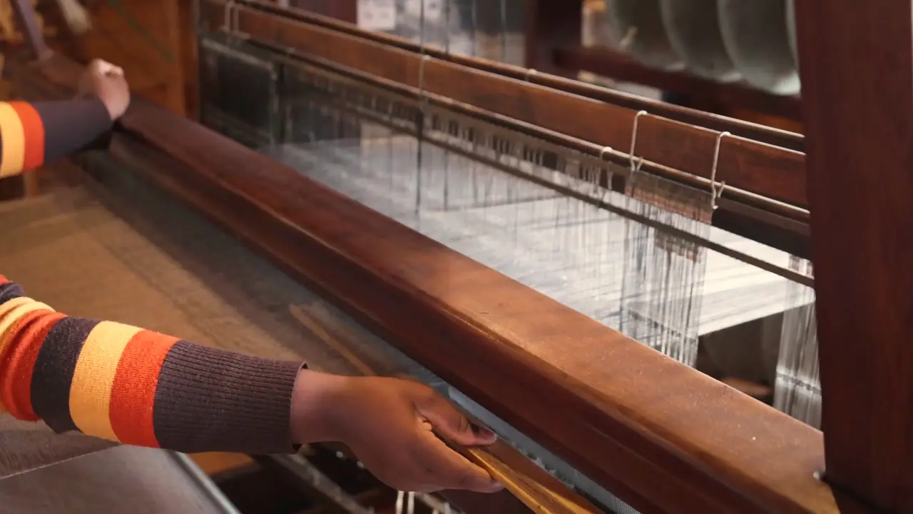 Example frame: a weaver’s hands at a wooden loom